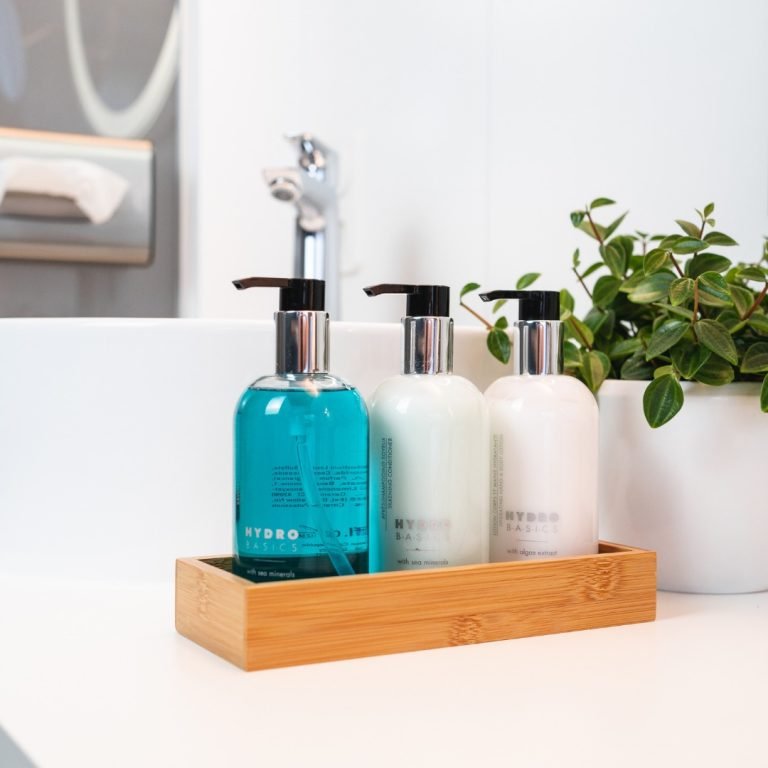Hydro Basics pump bottles in a wooden tray beside a bathroom sink