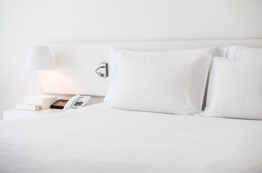 Hotel bed with white pillows and a bedside lamp