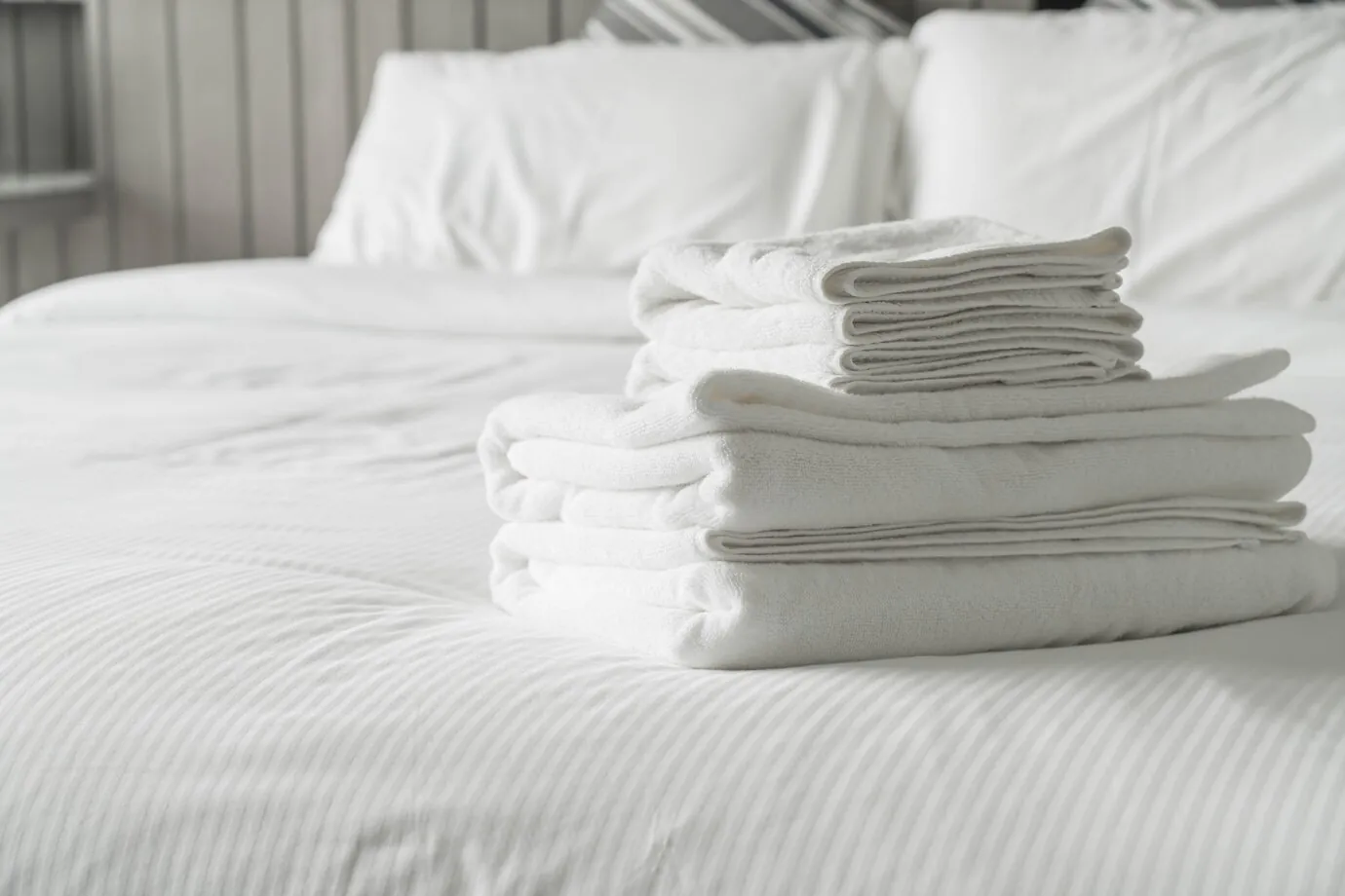 Folded white towels on a hotel bed with white linen