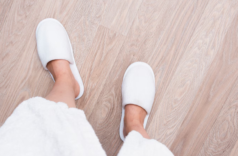 Guest wearing white hotel slippers on a wooden floor